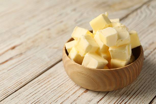 istock Tasty butter cubes in bowl on light wooden table. Space for text 2206940977