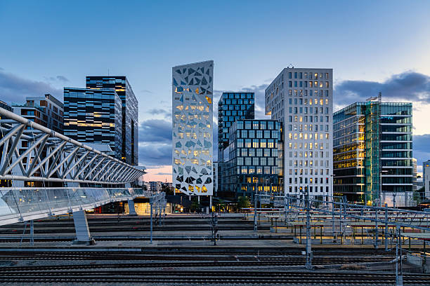 Twilight over downtown Oslo, the capital city of Norway close to Pedestrian Bridge over rails of central railway station. Illuminated modern buildings and skyscapers at dusk. Cityscape from elevated walkway in late summer. Oslo, Norway, Scandinavia