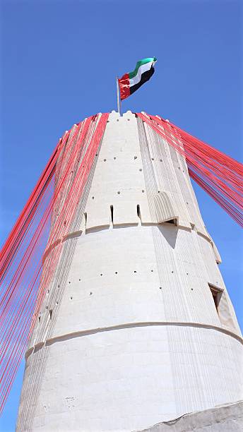istock Uae flag billowing atop whitewashed traditional tower, red ribbons fluttering, symbolizing national pride against vibrant azure backdrop 2206947274