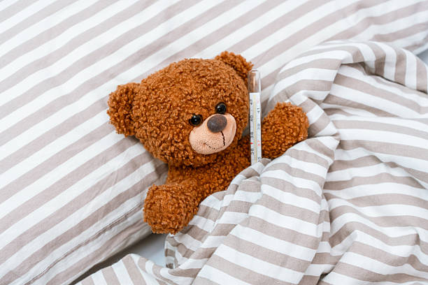 istock A bear toy with a thermometer under its arm is lying in bed under a blanket on an isolated background, 2206950664