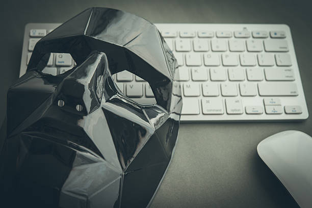 Black scary half face mask, keyboard and mouse on gray table background in dark tone. Hacker, cybercrime, romance scam and online security concept.