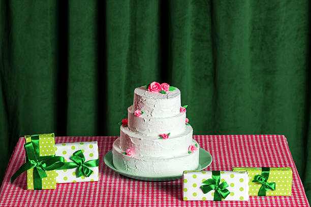 A multi-tiered cake and gift boxes on a checkered tablecloth on a background of green velvet curtains