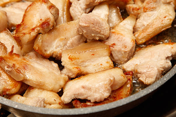 A pan of pork chops is cooking on a stove. The meat is browned and crispy, and the pan is full of grease