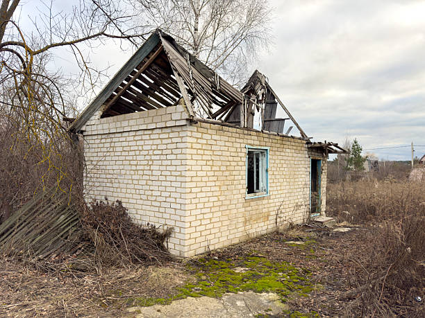 A dilapidated old house with a broken roof and a window. The house is surrounded by trees and he is abandoned