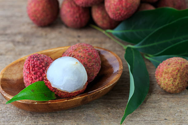 Fresh Lychee Fruit with Green Leaves on Wooden Plate on Rustic Table Background
