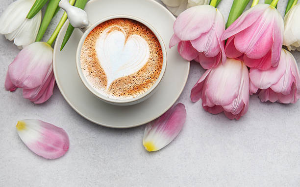 istock Cappuccino with heart shaped foam and pink tulips bouquet on grey table 2206957252