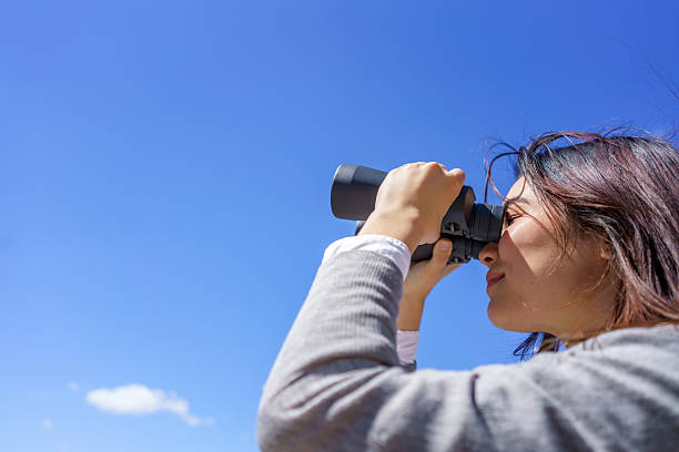 istock Young japanese woman looking through binoculars at a clear blue sky 2206957301