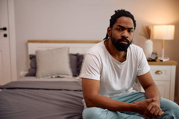 istock Distraught black man sitting on a bed and looking at camera. 2206958966