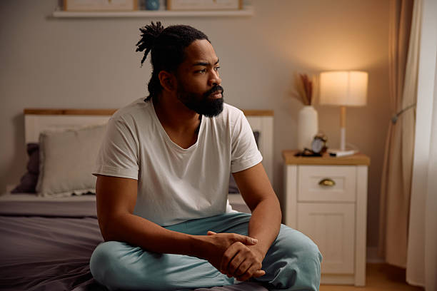 Pensive black man thinking of something while sitting alone in bedroom.