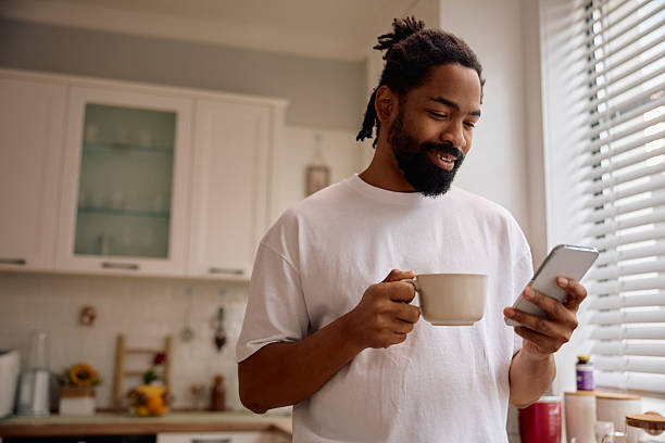 istock Happy black  man using cell phone while drinking morning coffee in the kitchen. 2206959131