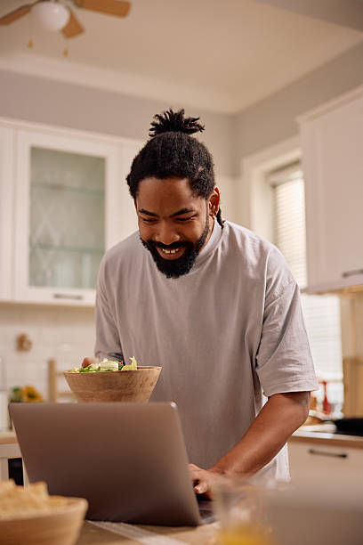 istock Happy black man using laptop while preparing food in the kitchen. 2206959269