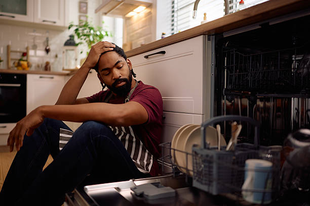 Black man man feeling upset about the dishwasher malfunctioning in the kitchen.