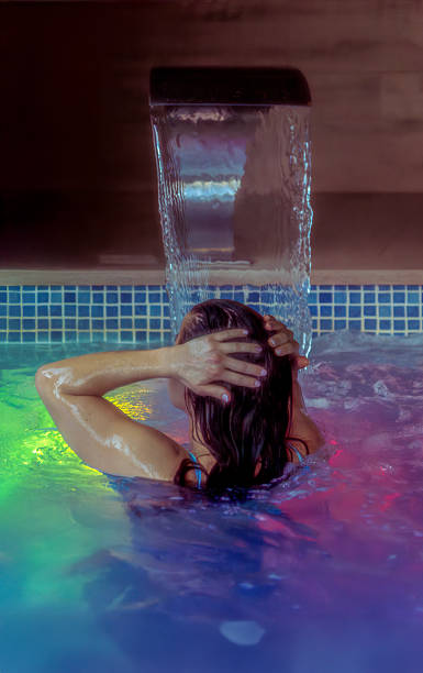 istock Woman relaxing, touching her hair under a waterfall in a spa with colored lights within the water. 2206966800