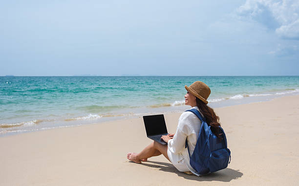 istock A female traveler using and working on laptop computer while sitting on the beach 2206972283