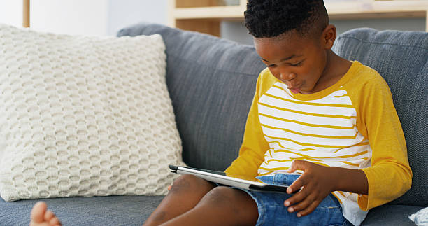 istock Tablet, home and African kid on sofa for reading ebook, learning app or streaming cartoon video. Relax, boy and child in living room on technology for entertainment, watch movies or play games online 2206972828