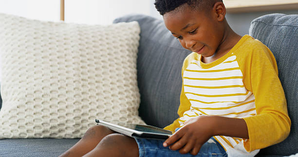 istock Tablet, home and African kid online on sofa for reading ebook, learning app or streaming cartoon video. Relax, boy and child in living room on technology for entertainment, watch movies or play games 2206972835