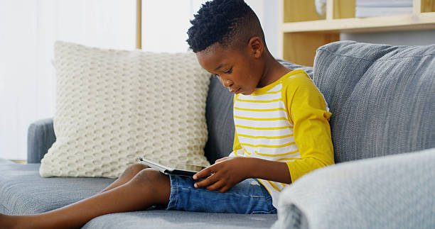 istock Tablet, home and child relax for reading ebook, learning app or streaming cartoon on sofa. African boy, kid and online in living room on technology to scroll entertainment, watch movies or play games 2206972886