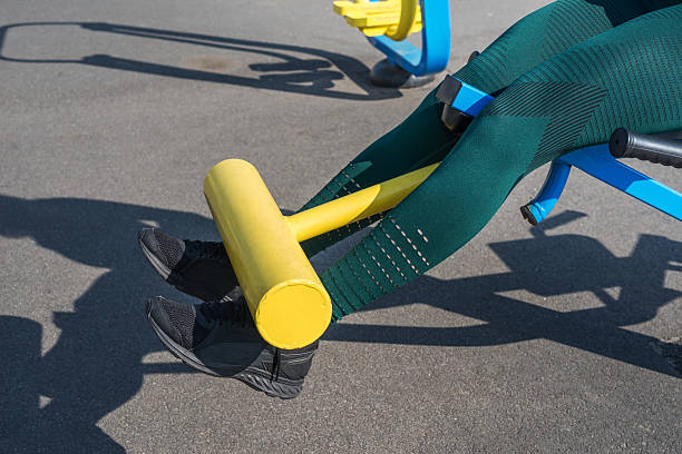 Female legs are trained on a simulator in the fresh air. The athlete's legs raise the dumbbell.