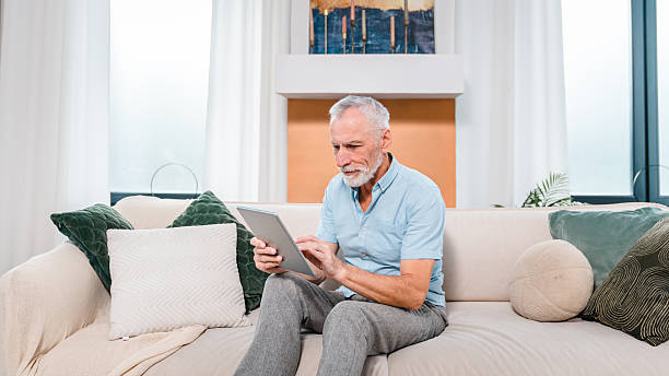istock Senior Man Using Tablet Inside Cozy Modern Living Room on Comfortable Sofa 2206974484