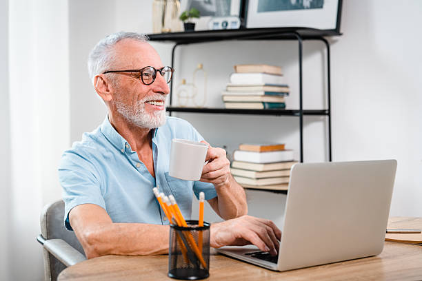istock Smiling Senior Man Using Laptop and Drinking Coffee at Home Office 2206974662