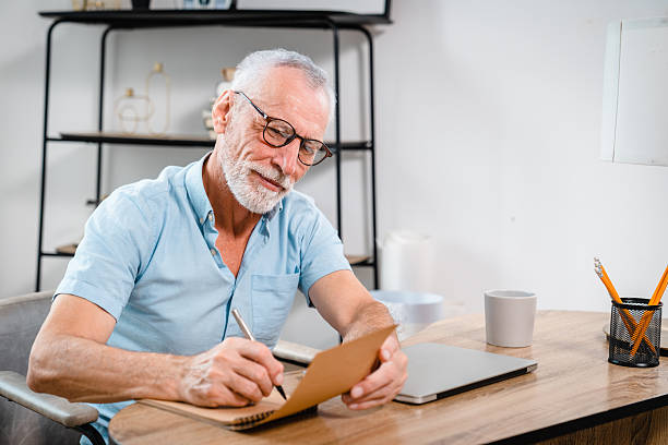 istock Senior Man Writing Notes at Desk in Modern Home Office 2206974689
