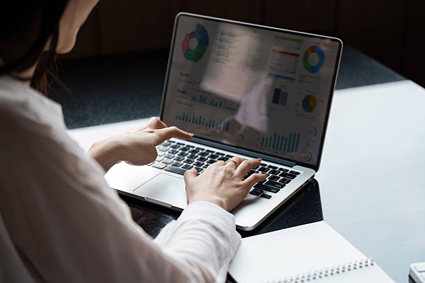 istock Focused Asian woman analyzing financial data on a laptop while taking notes in a modern office. 2206974855