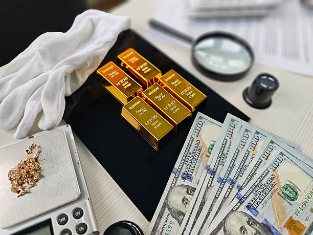 istock Gold bars, cash and a magnifying glass arranged on a table 2206976707