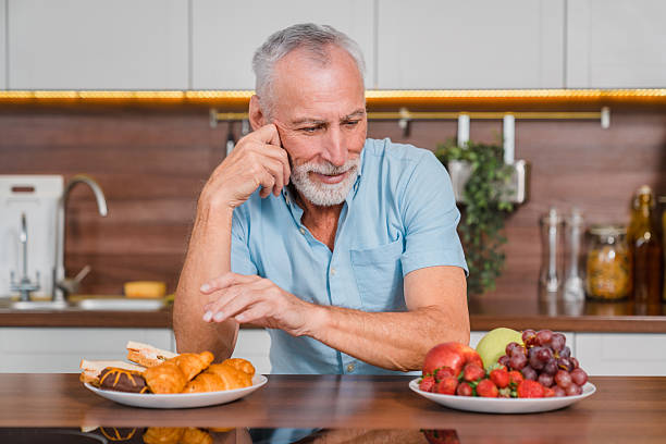 istock Man Deciding Between Healthy Fruits and Pastries in a Kitchen Environment 2206977033