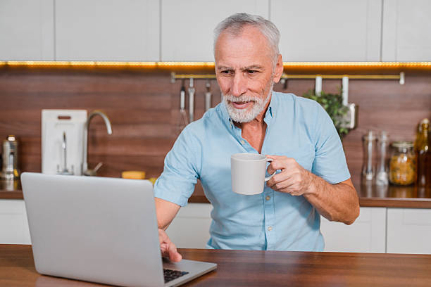 istock Senior Man Enjoying Coffee While Using Laptop at Home Kitchen Counter 2206977075