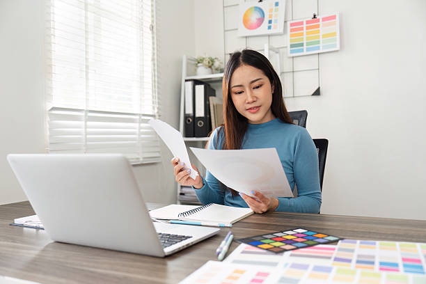 istock Design Review and Color Analysis. A creative professional examining design papers and color charts in a vibrant workspace. 2206977488