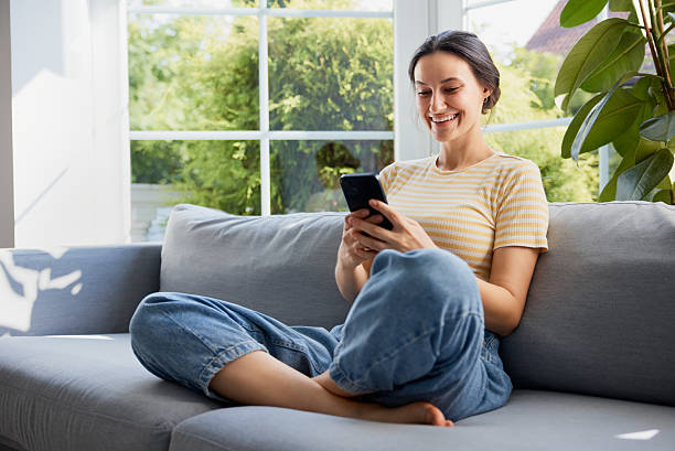 istock Woman with mobile phone sitting on sofa at home 2206977856