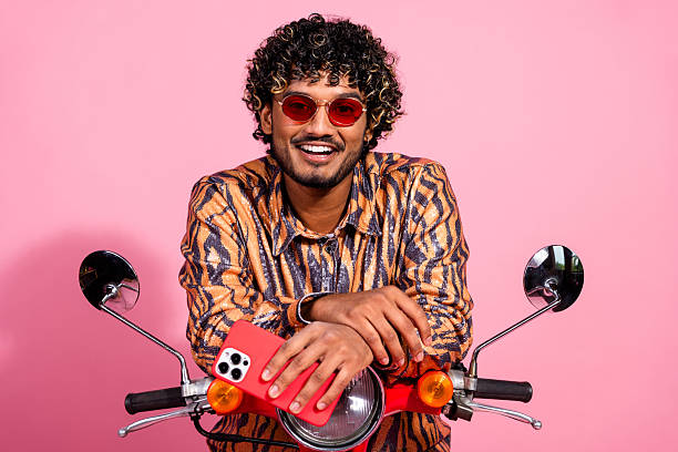 istock Stylish young man posing on a scooter against a vibrant pink background, showcasing contemporary fashion and casual elegance 2206979327