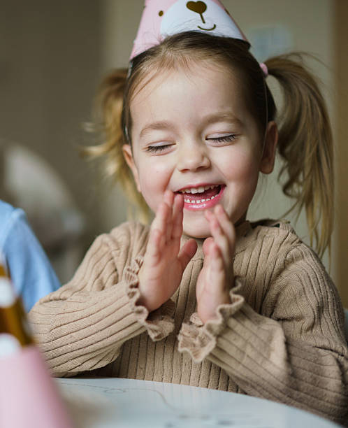 Cute little girl with a birthday hat claps her hands during a birthday celebration at home