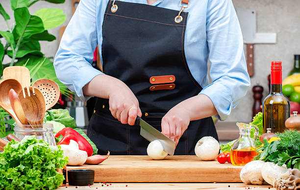 istock Home cook cuts white onion into half with knife in cozy kitchen with wooden table, kitchenware, vegetables, herbs and ingredients for cooking. Healthy vegan food, culinary, recipes, blogging 2206979679