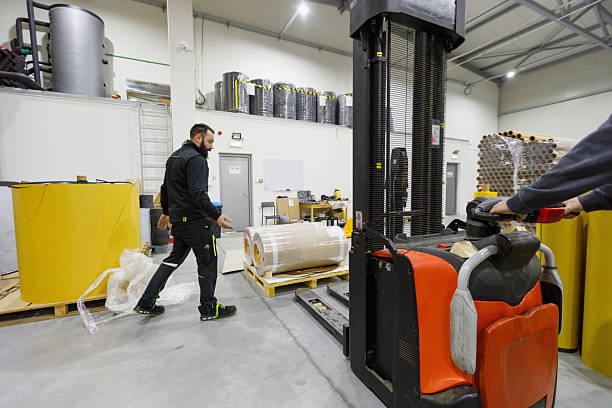 istock Man holding plastic wrap in distribution warehouse, coworker lifting palette with forklift 2206983057