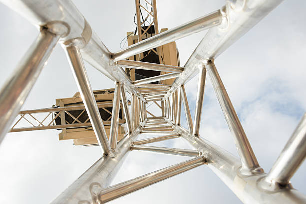 Striking low-angle bottom-up view of a steel truss framework with diamond-shaped beams welded seamlessly. Set against a partly cloudy sky, this image captures the elegance and strength of truss design, ideal for construction, engineering, and stage setup visuals.