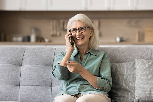 istock Older woman sits on sofa talking on her phone 2206984623