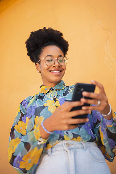 istock Smiling woman using smartphone against yellow background wearing patterned floral blouse 2206986550