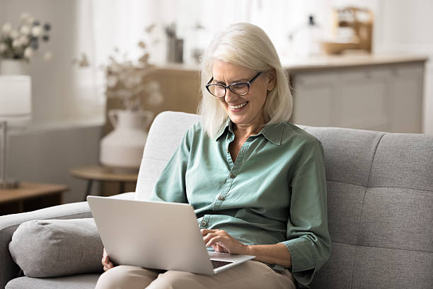 istock Happy older woman sitting on couch with modern laptop 2206987874