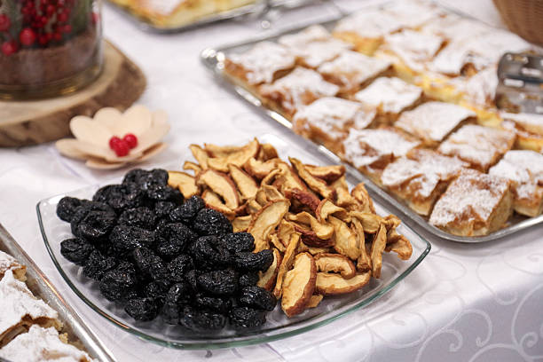 A beautifully arranged dessert table featuring powdered sugar pastries, dried plums, dried apples, and a decorative candle centerpiece at a festive event.