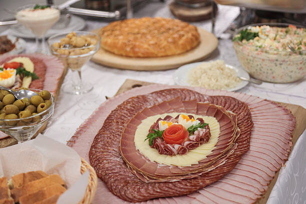 A beautifully arranged cold cuts platter featuring ham, salami, and cheese, garnished with decorative eggs and vegetables, served on a banquet table.
