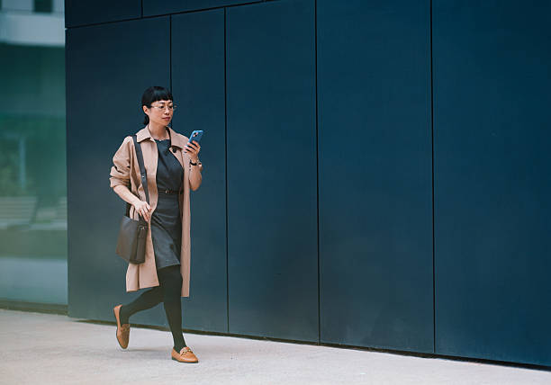 Stylish Businesswoman Walking in Urban Setting While Using Smartphone
