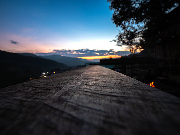 Shot of the surface of a wooden terrace on a high mountain with an orange-pink sky in the background at dusk. The last light of the day shines down on the wooden floor, creating a warm and romantic atmosphere, perfect for relaxing and enjoying the beautiful scenery.