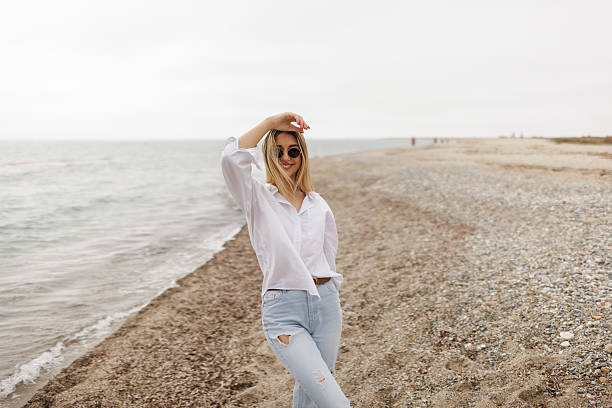 Portrait of cheerful young woman in white shirt and jeans standing on the beach