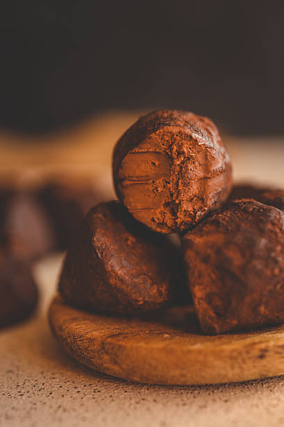 Stack of chocolate truffles on a wooden plate, one with a bite taken out, showing smooth filling and rich texture, with warm background lighting