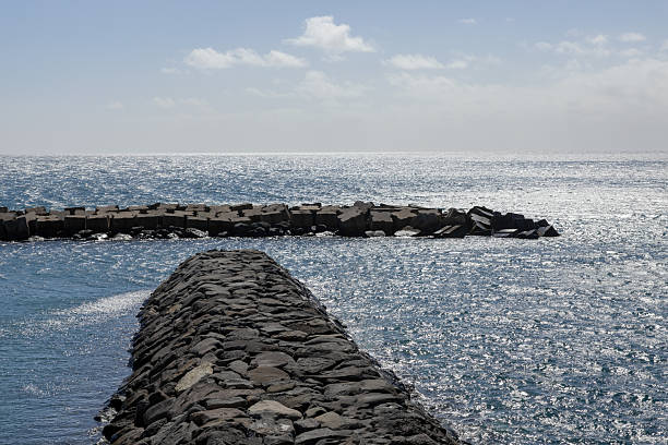 Black stone piers in the Atlantic Ocean with reflected sunlight and glare