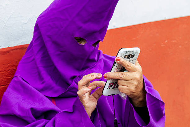 Quito, Pichincha, Ecuador - April 15, 2022: Cucurucho, check his smartphone while waiting in the line for the procession during a Holy week.