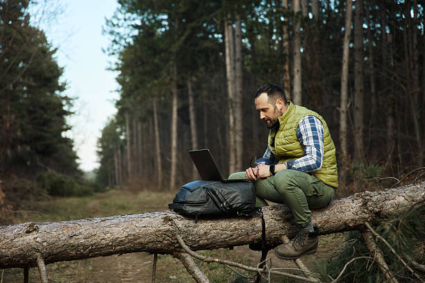 istock A young and handsome man is sitting on a fallen tree trunk and working on his laptop computer. 2207022440
