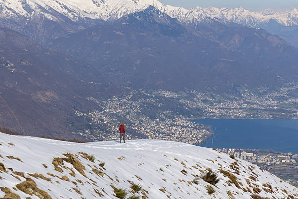 Traveler walking along snowy mountain, enjoying stunning view of alpine valley. Adventurous scene capturing serene snow-covered landscape. Perfect for travel and nature concepts.