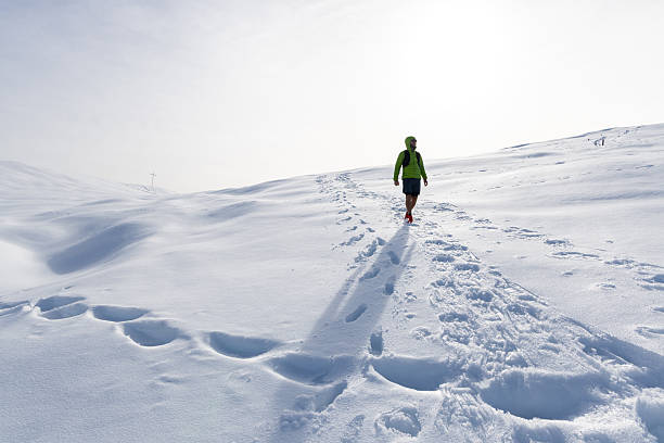 Man in a green jacket with a backpack standing on a snowy hill. Winter trekking activity. Outdoor adventure in pristine snowy environment.